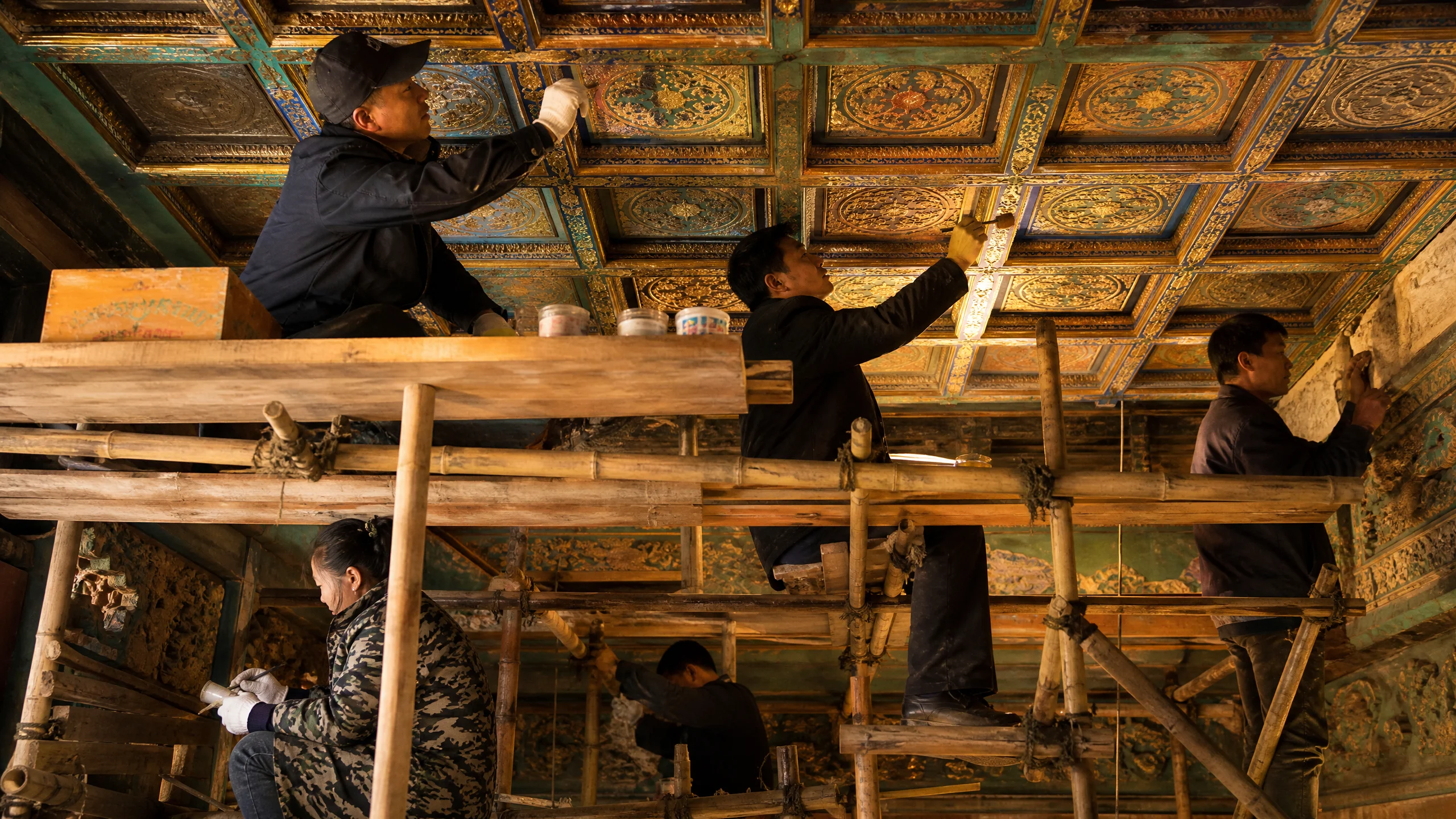 古建筑​修复工程现场，工匠在脚手​架上修复藻井彩画